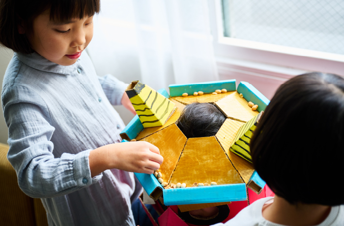 ダンボールで作った鬼のお面に豆を入れるゲームを楽しむ子ども。